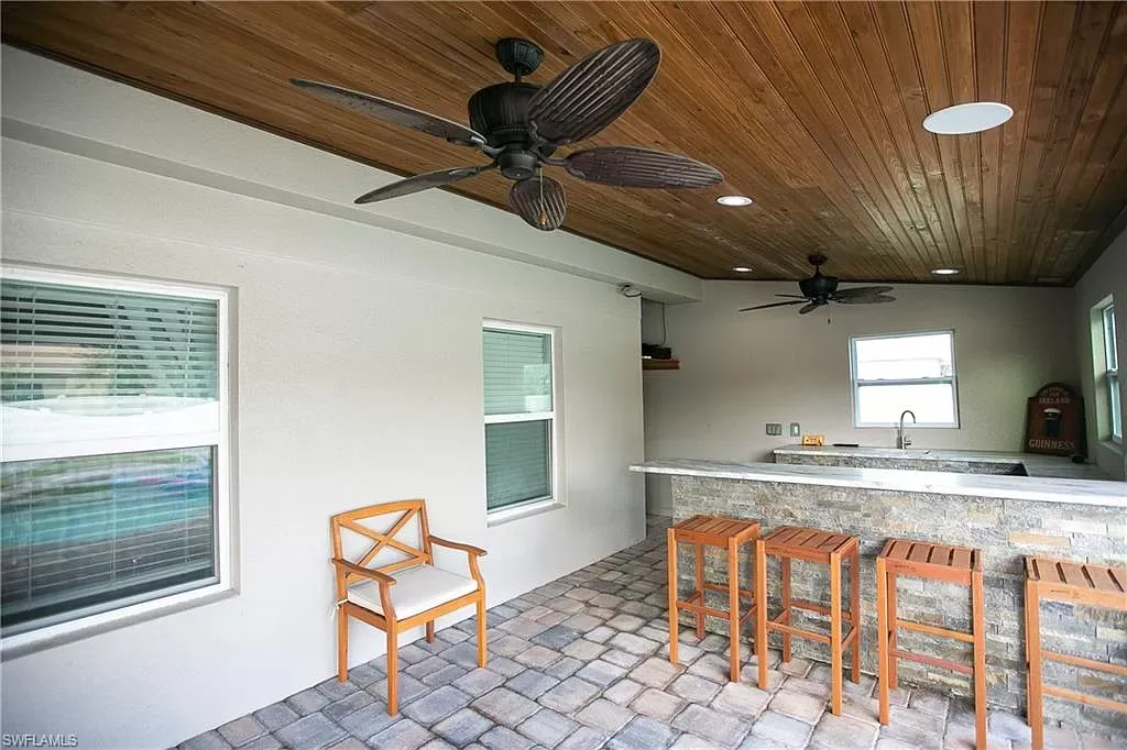 Outdoor kitchen with stone bar, wooden stools, and ceiling fans.