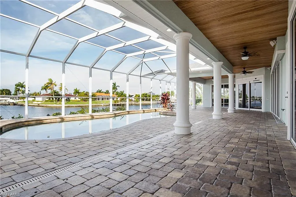 Patio with pool, view of lake, brick flooring, white columns, screened ceiling.