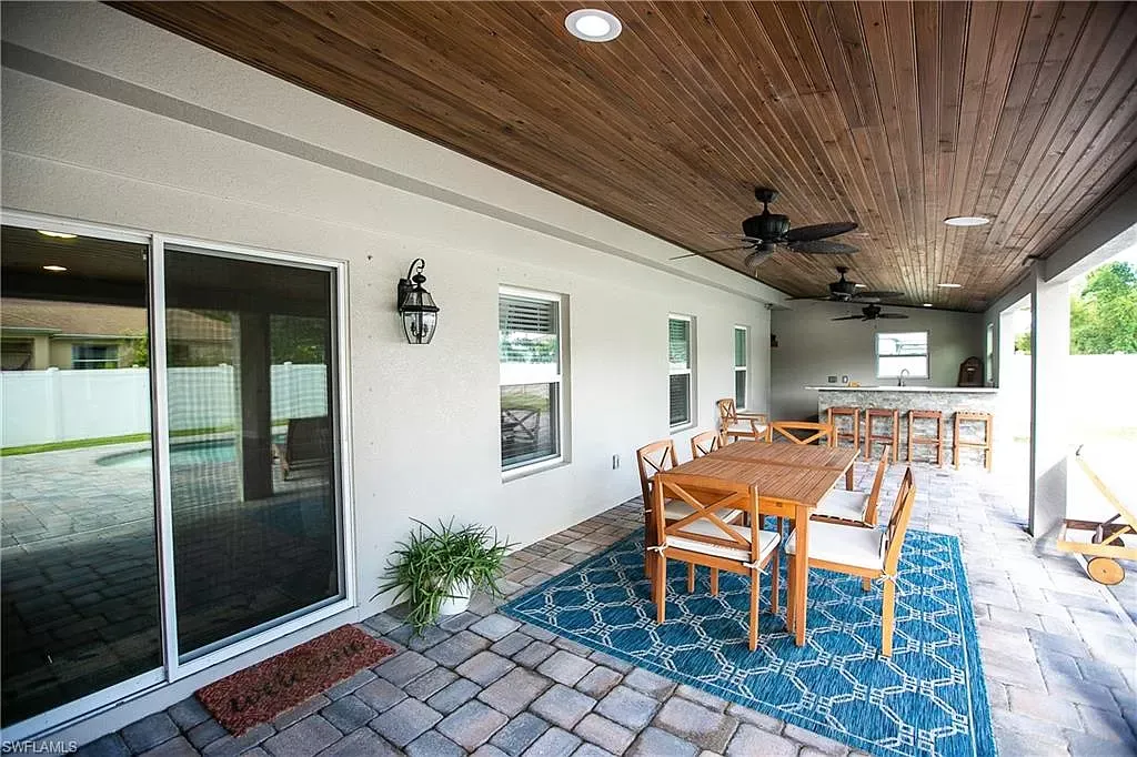 Covered patio with wooden ceiling, dining table, and an outdoor kitchen.