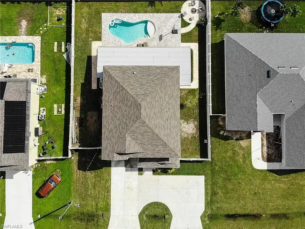 Aerial view of a house with a pool, backyard, and driveway surrounded by neighboring houses.