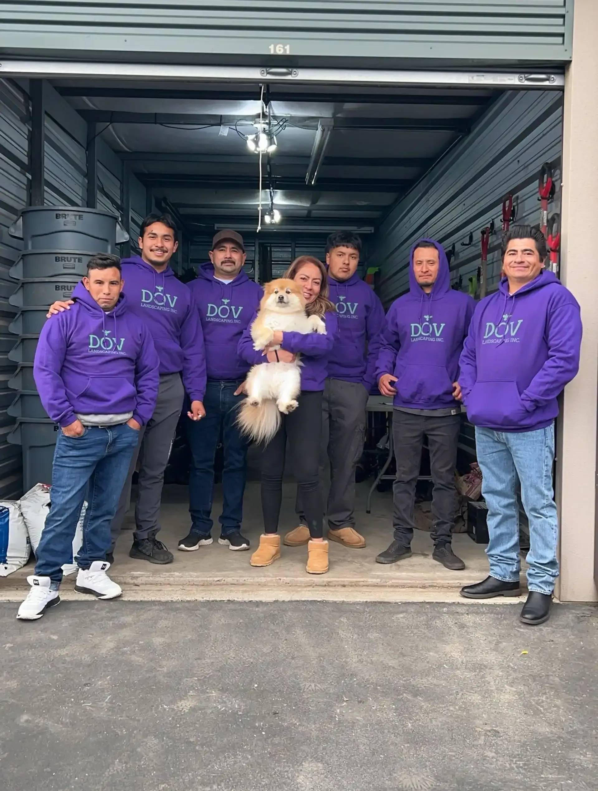 A group of people in purple hoodies are posing for a picture with a woman holding a dog.