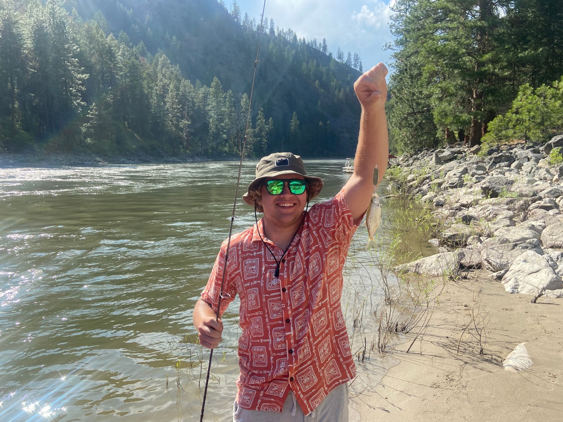 A man wearing sunglasses and a hat is holding a fish in his hand.