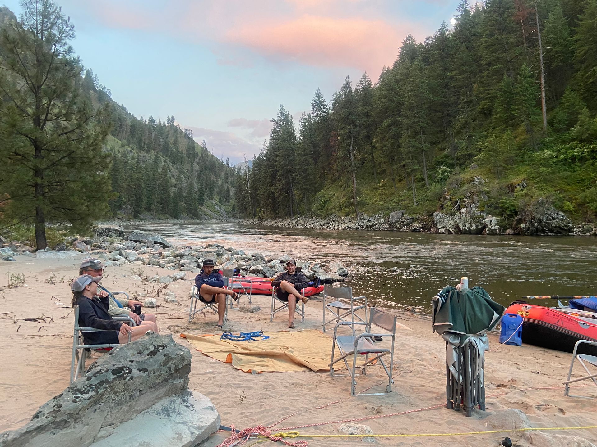 A group of people are sitting on the beach near a river.
