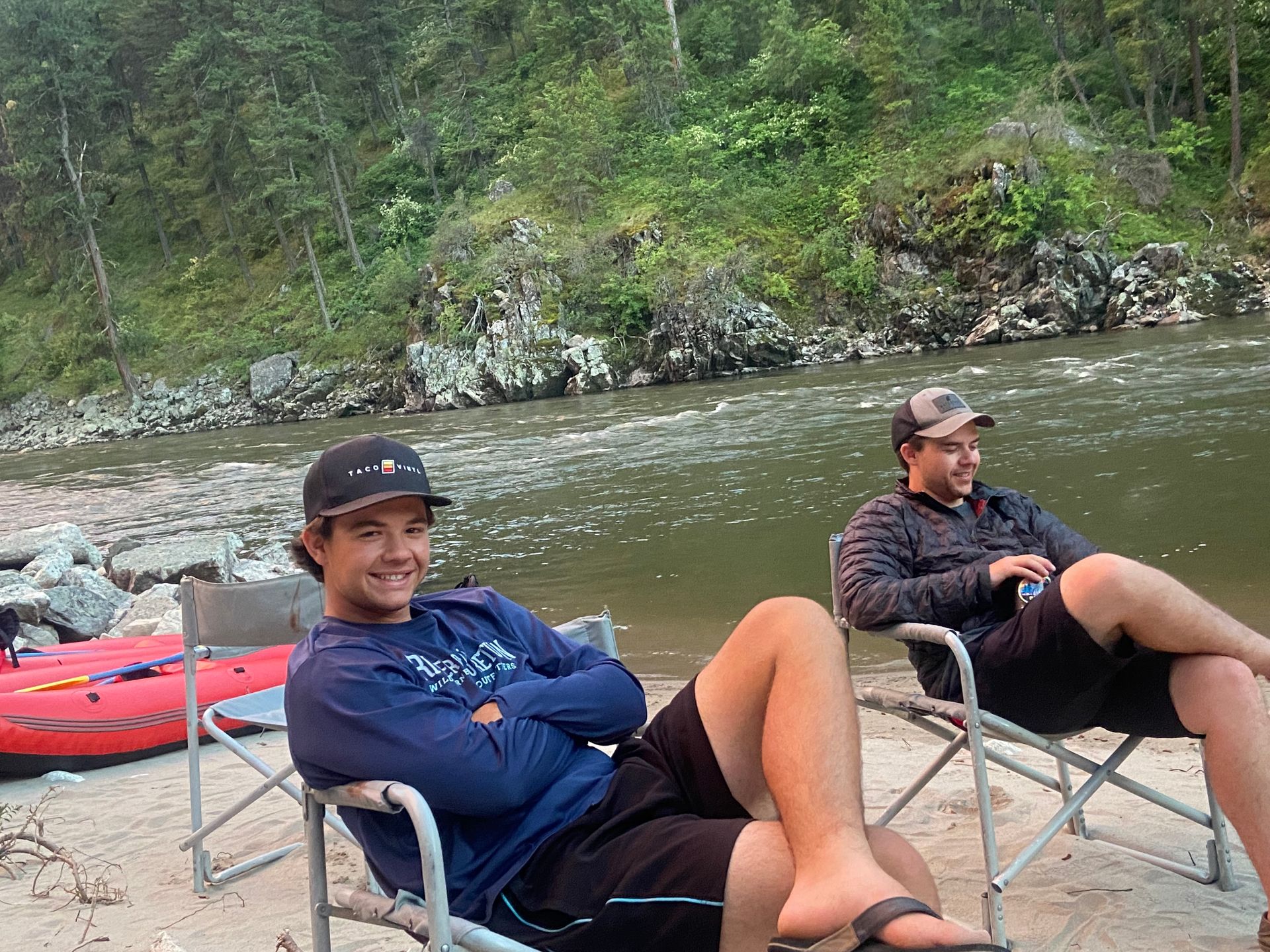 Two men sitting in camping chairs next to a river.