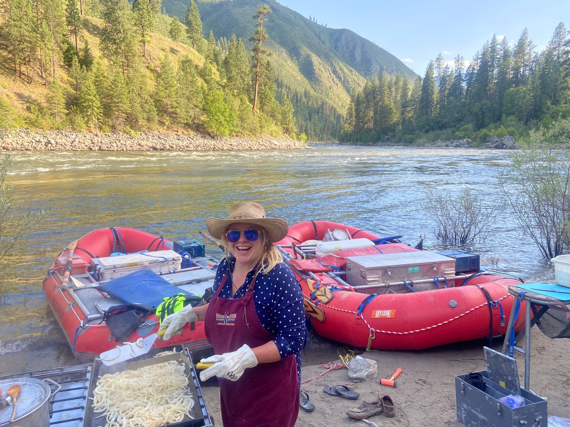 A woman is standing in front of two rafts on the shore of a river.