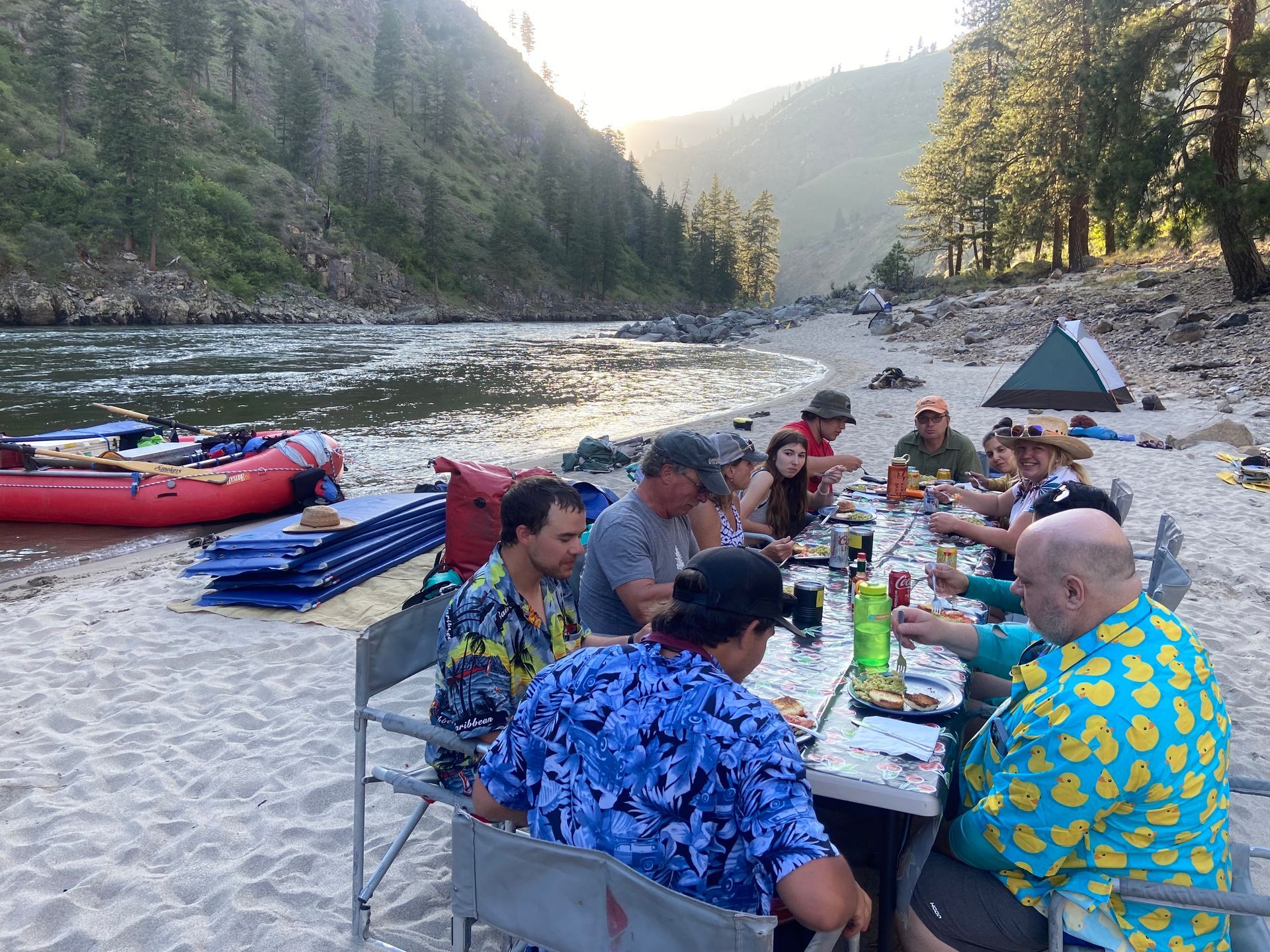 A group of people are sitting at a long table by a river.