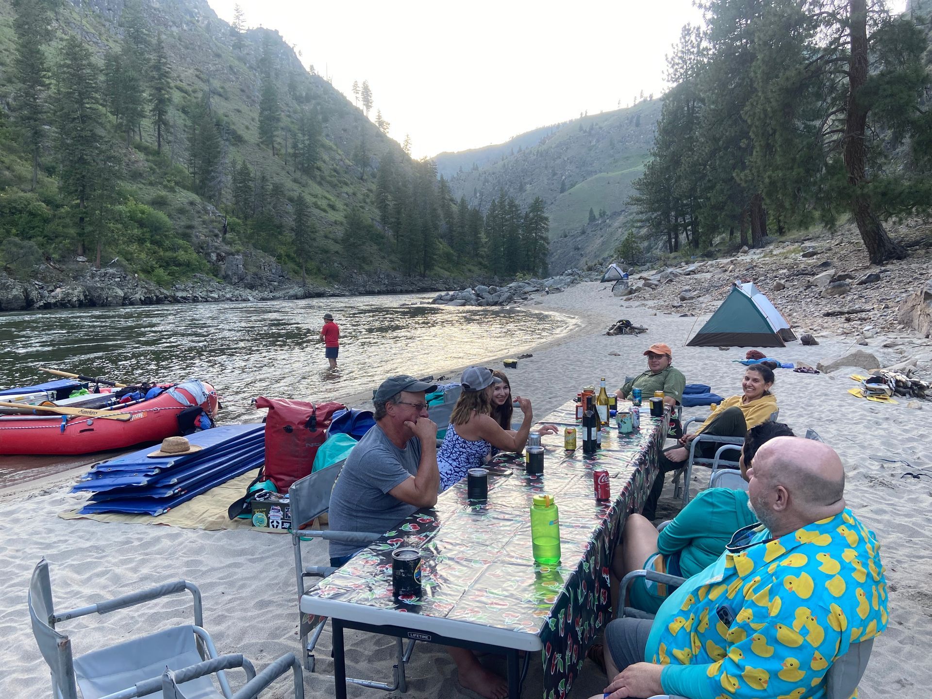 A group of people are sitting at a table by a river.