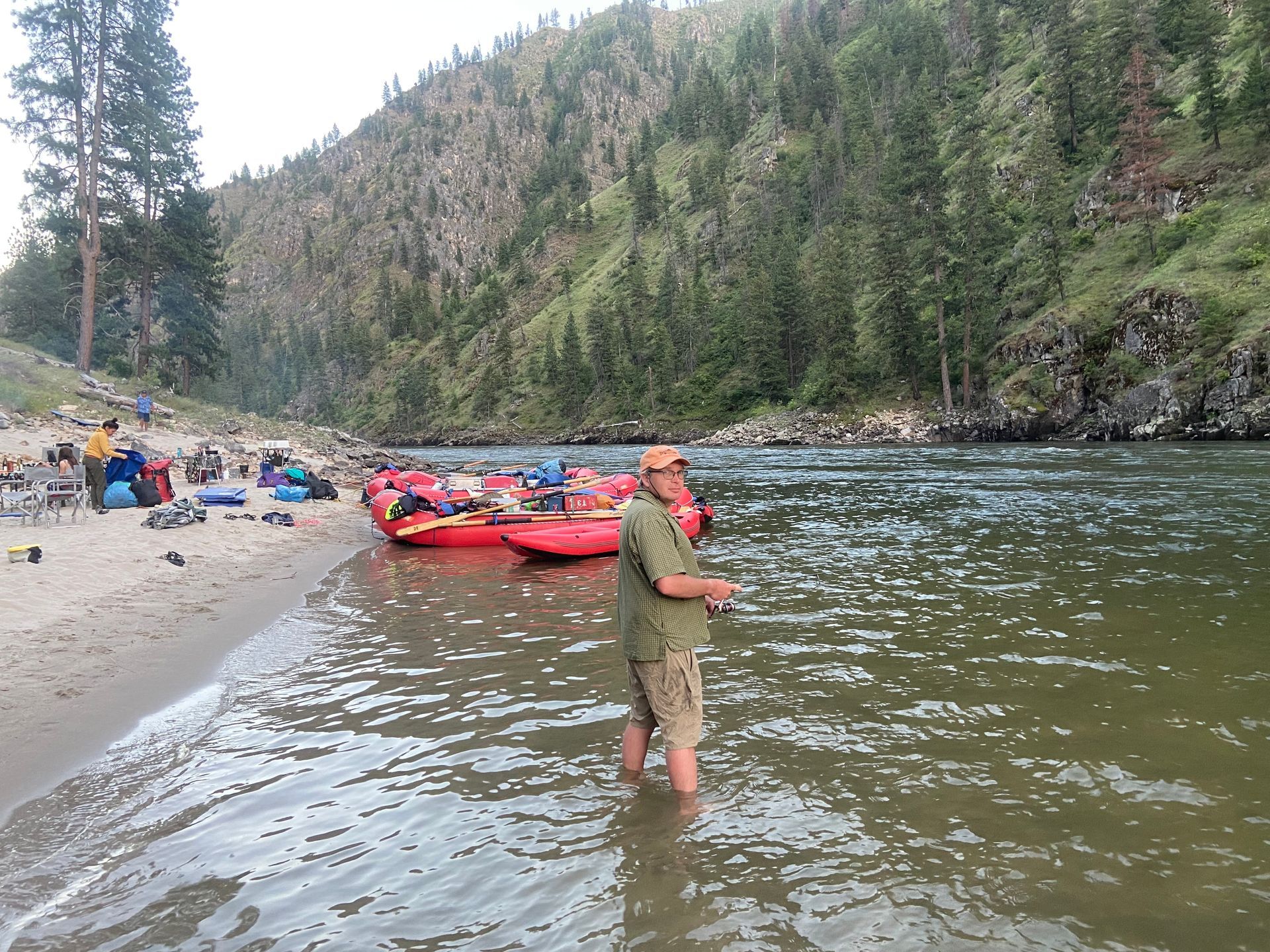 A man is fishing in a river near a beach.