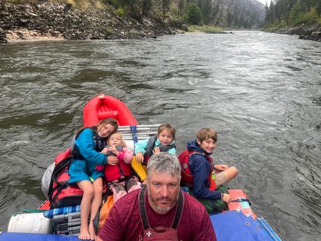 A man and three children are sitting in a raft on a river.