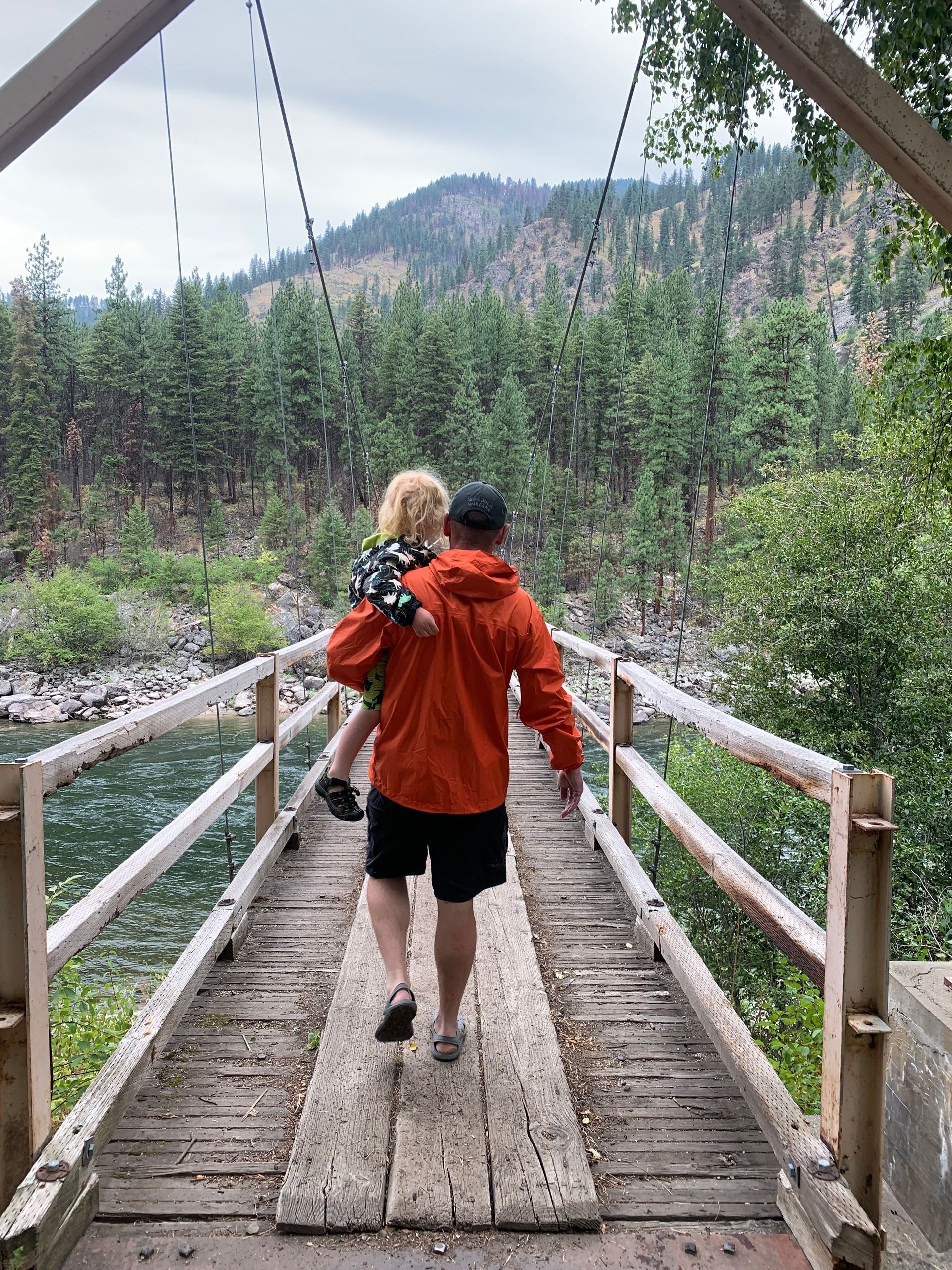 A man is carrying a child on his shoulders across a wooden bridge.