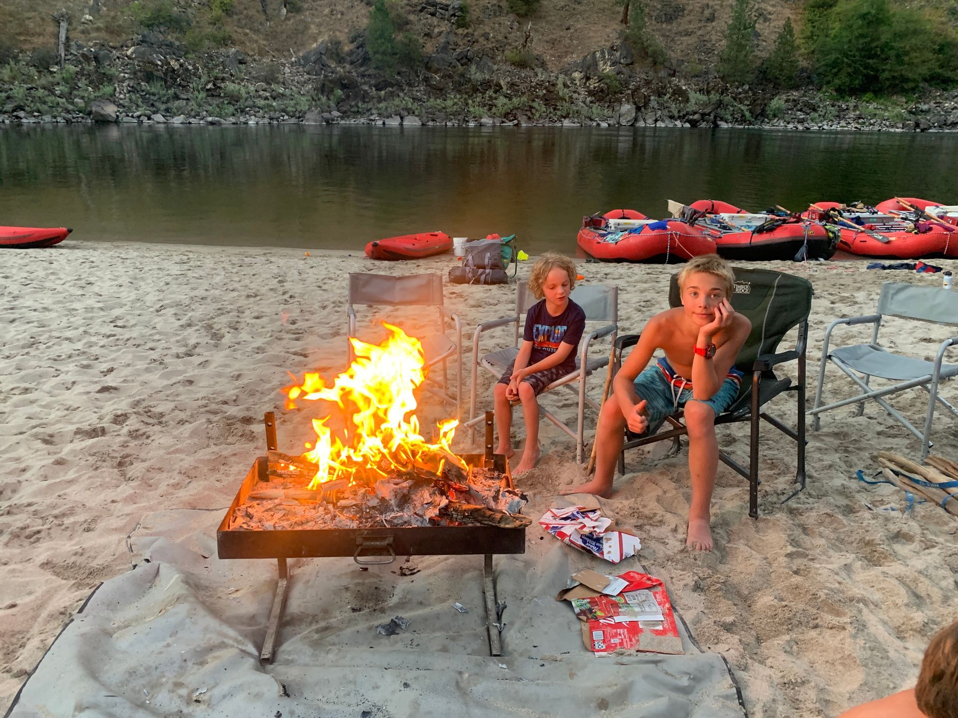 A group of children are sitting around a fire on the beach.
