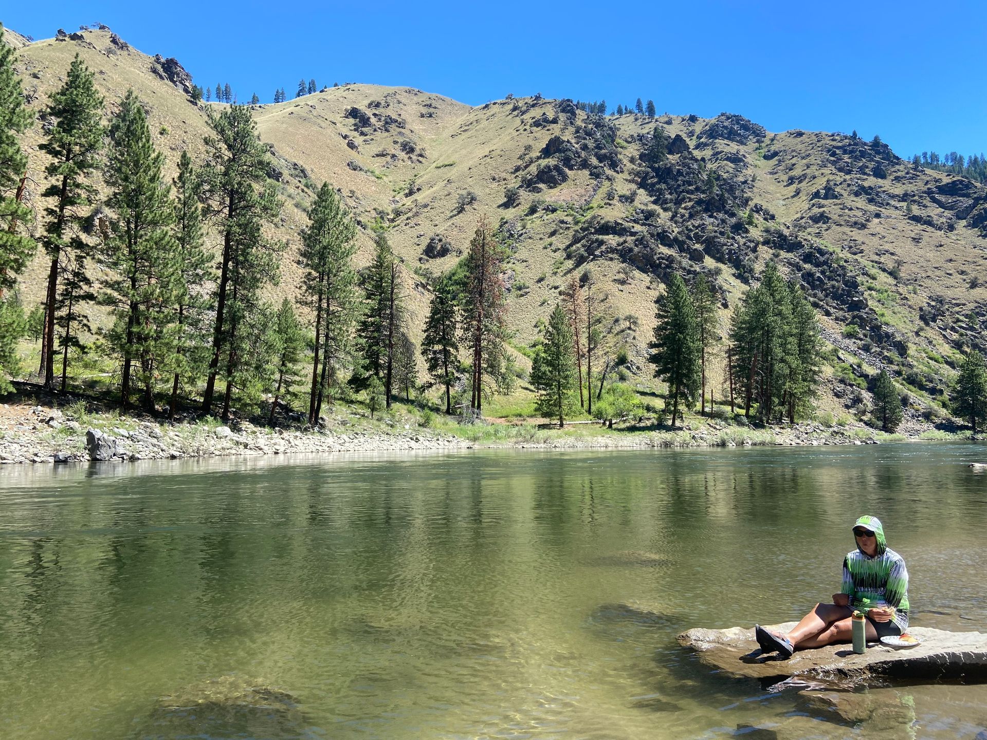 A person is sitting on a rock in the middle of a lake.