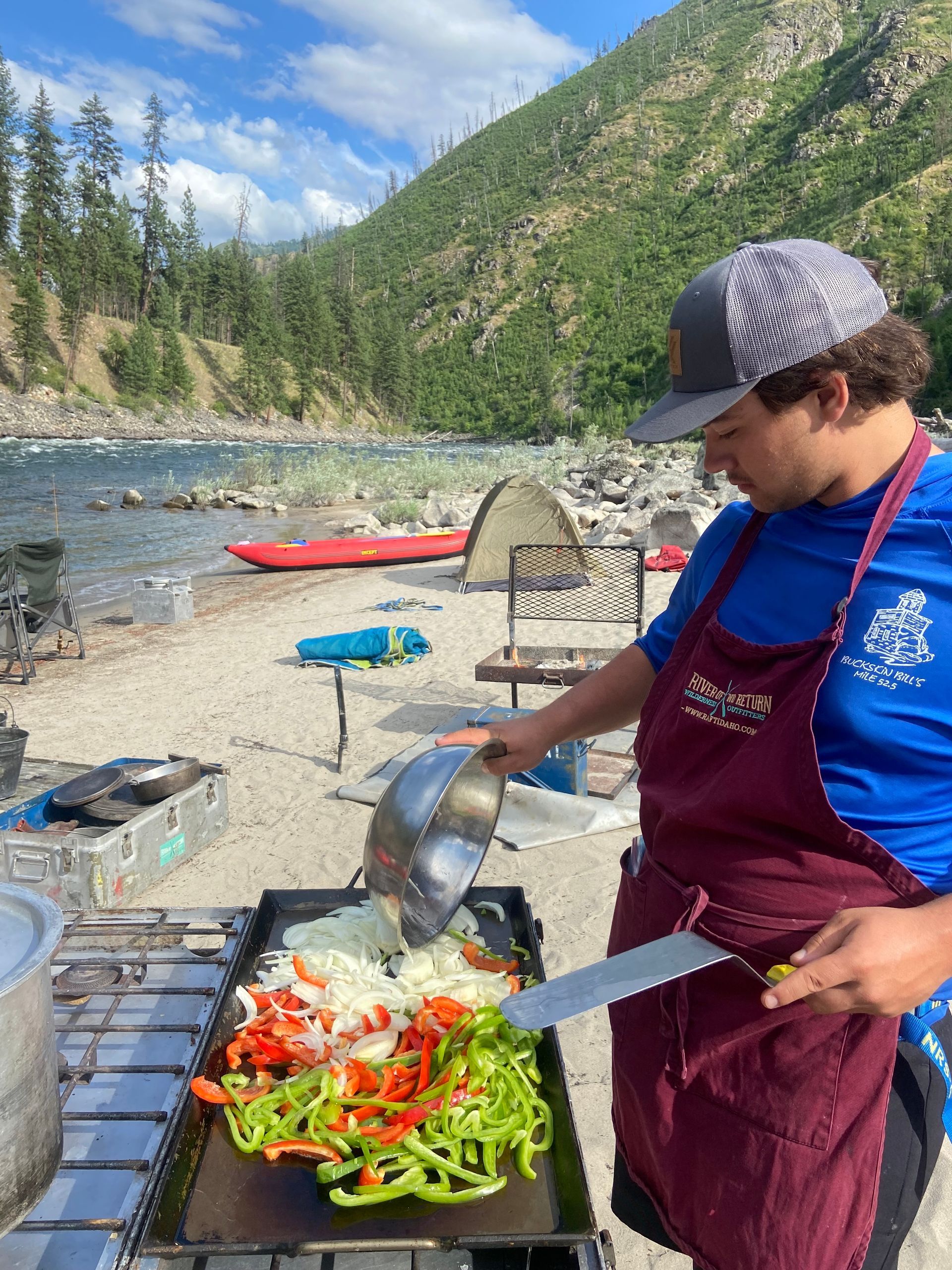 A man is cooking vegetables on a grill on the beach.
