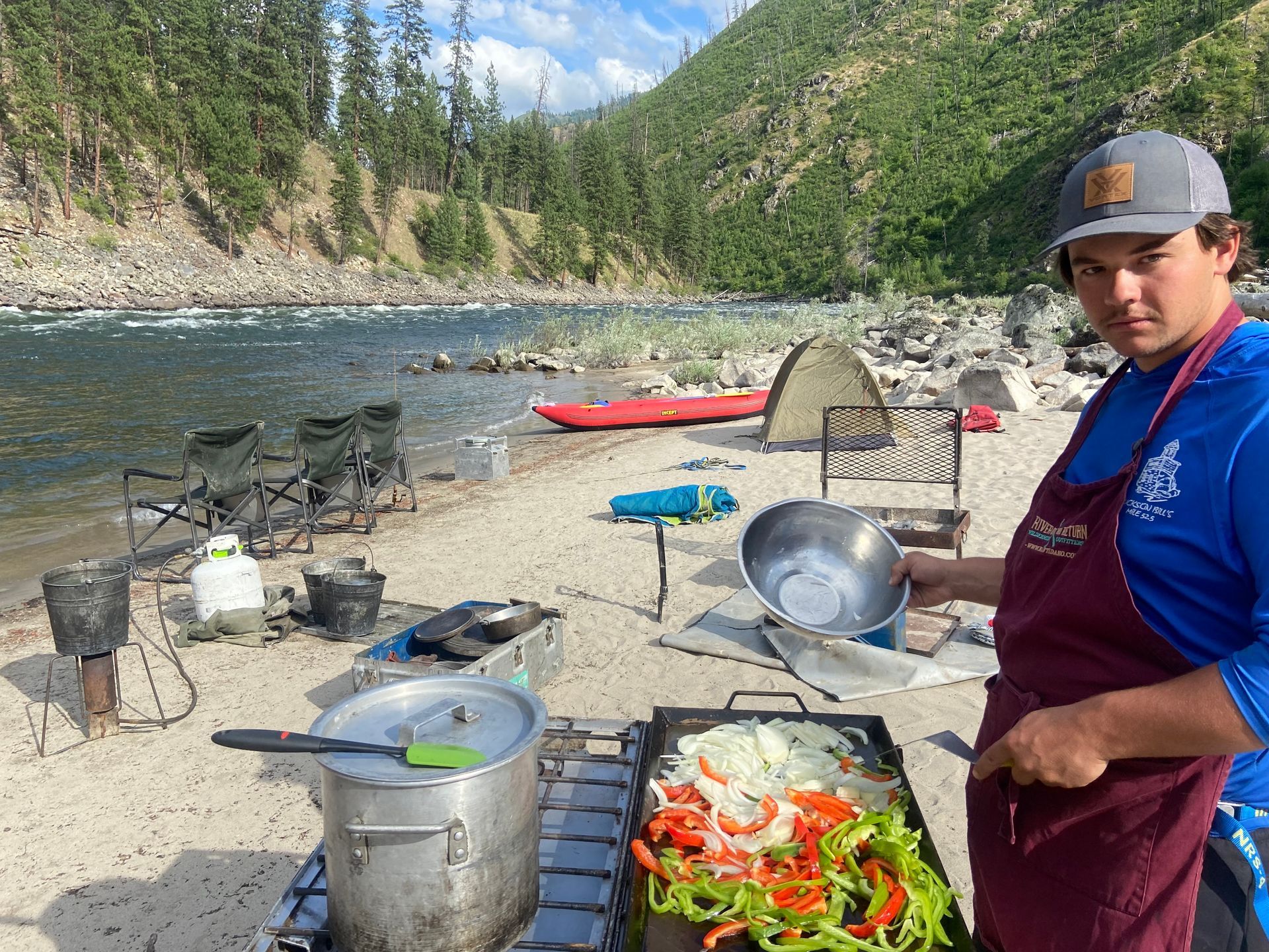 A man is cooking vegetables on a grill on the beach.