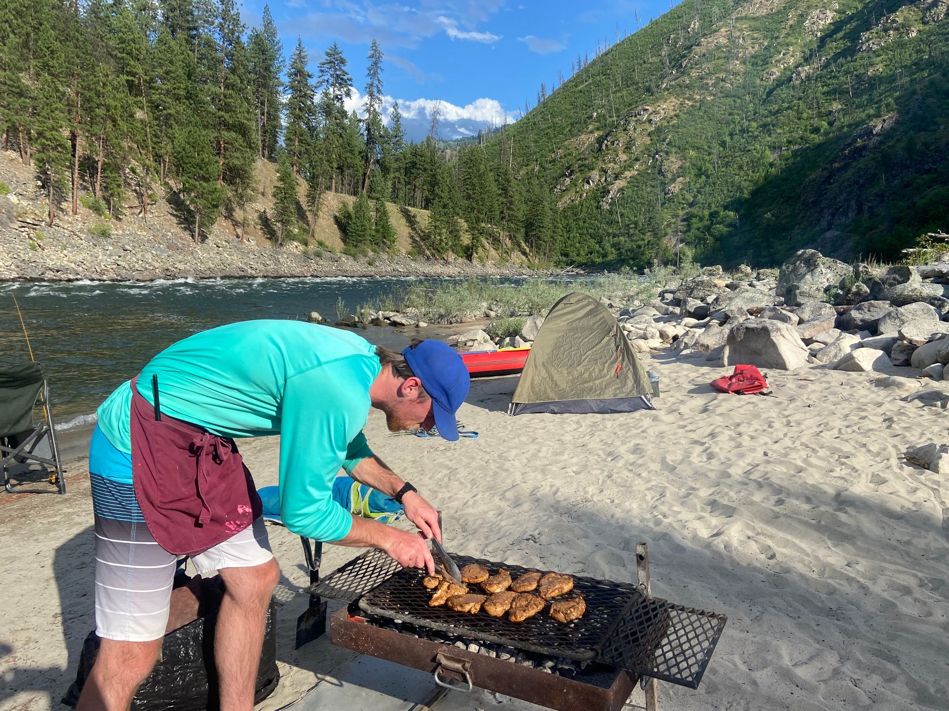A man is cooking food on a grill on the beach.