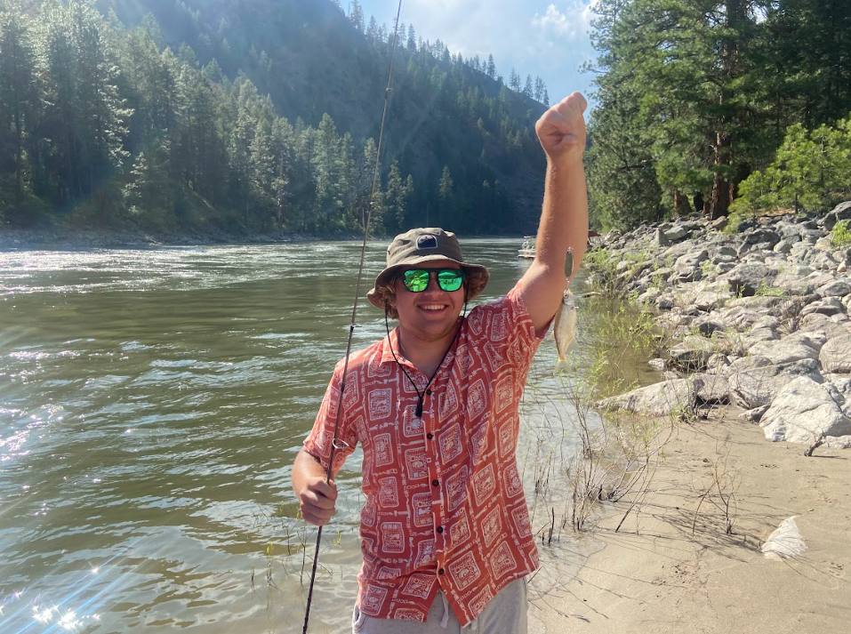 A man is fishing in a river and holding a fish in his hand.