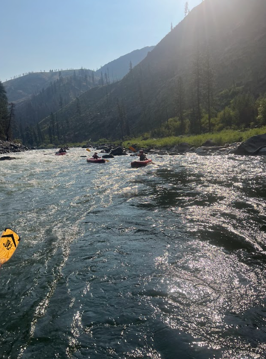 A group of people are kayaking down a river with mountains in the background