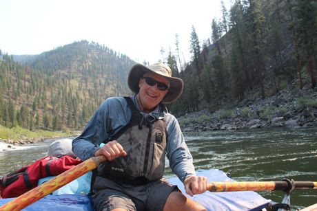 A man is sitting in a raft on a river holding a paddle.