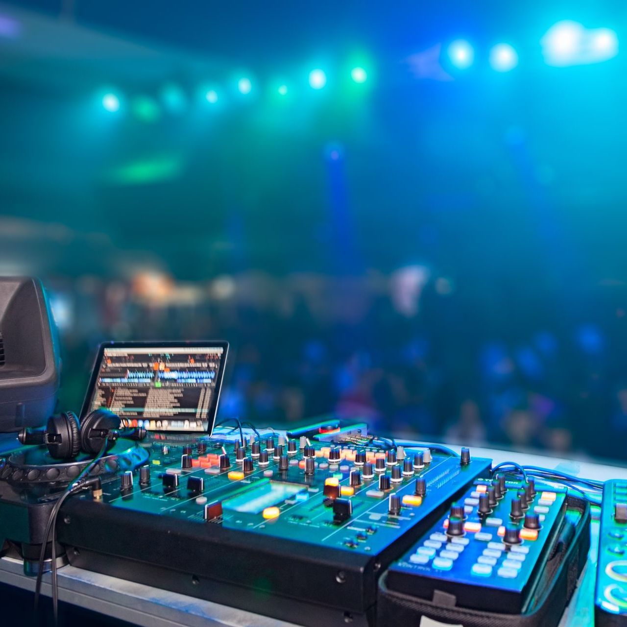 A dj 's mixer is sitting on a table in front of a crowd.