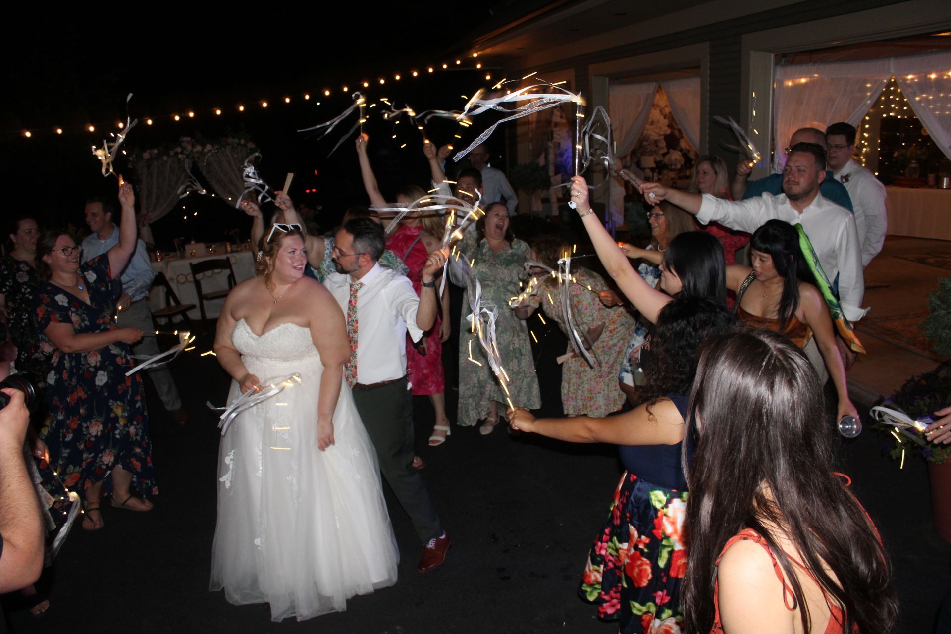Wedding couple surrounded by guests holding sparklers, celebrating outdoors at night.