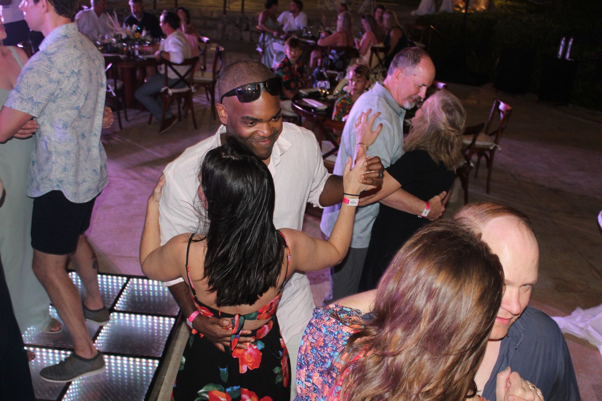 People dancing at an outdoor event with a dance floor. A couple dances in the center, other couples around them.