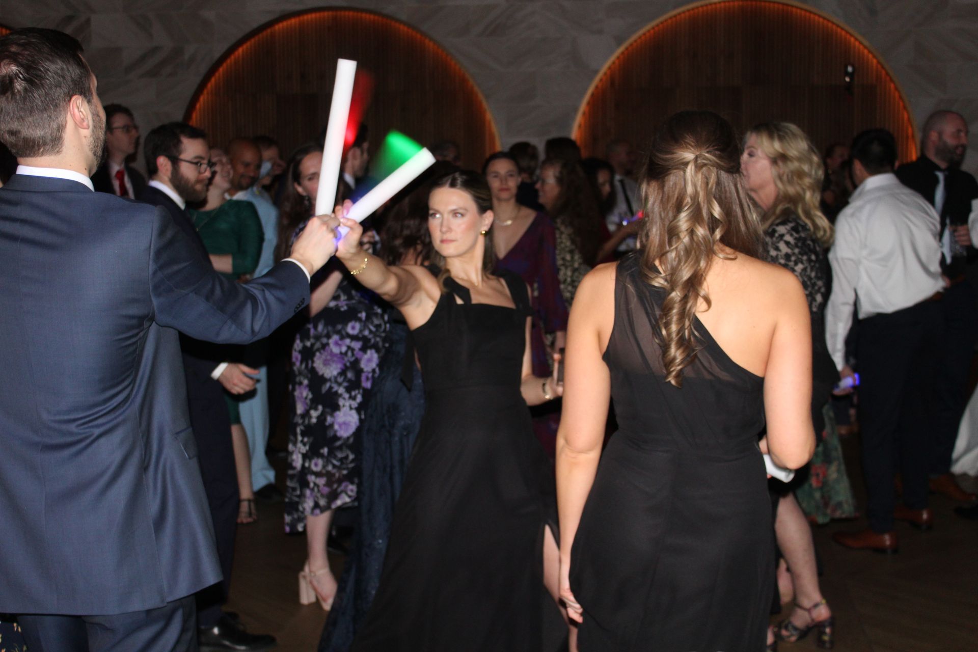 People dancing at a party, one holding light-up wands. Others wear formal attire.