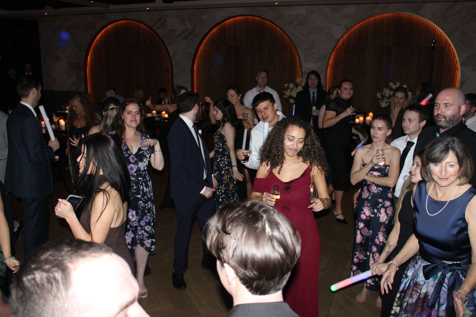 People dancing at a party in a dimly lit room with arched wall features.