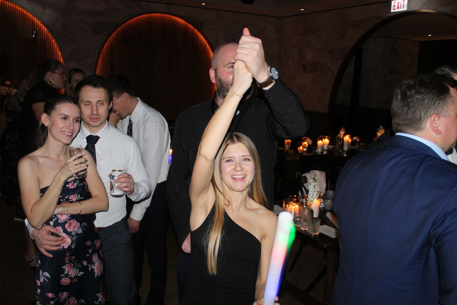 People at a party, woman holding up a glow stick, man holding her hand, others in background.