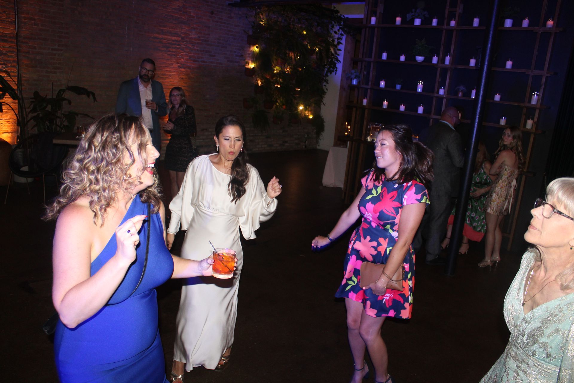 People dancing at a party with warm lighting; one woman holds a drink, others smile.