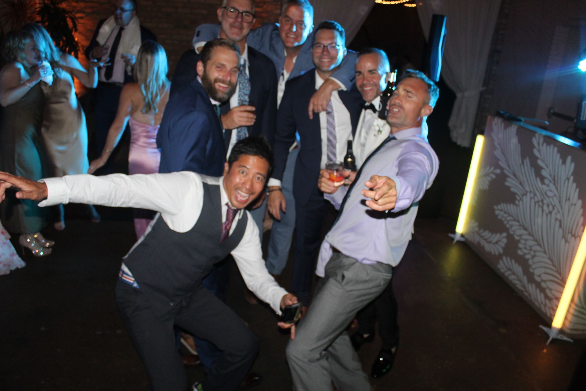 Group of men posing for a photo at a party, some holding drinks, one pointing at the camera.