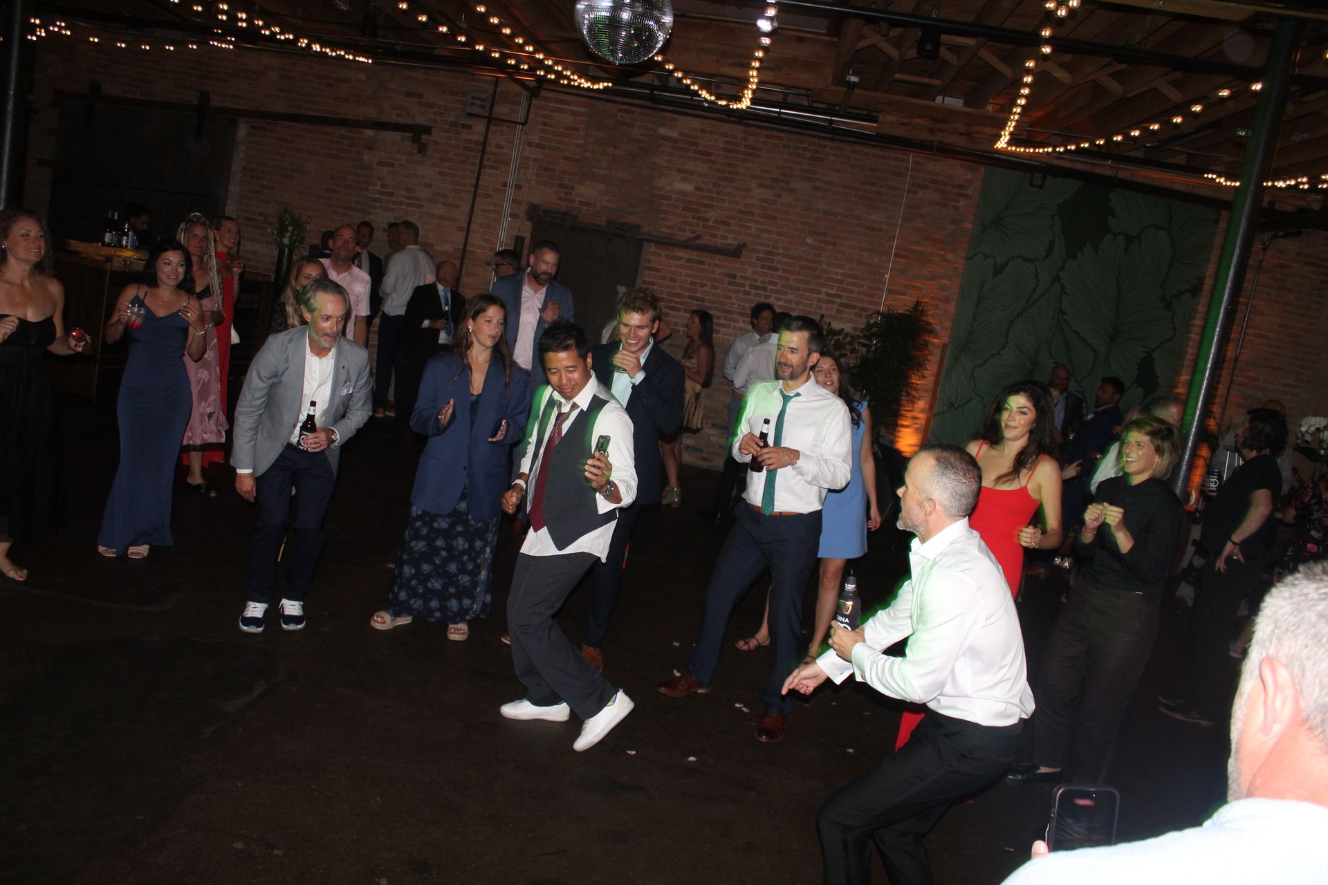 People dancing at a party in a dark room with string lights and a disco ball.