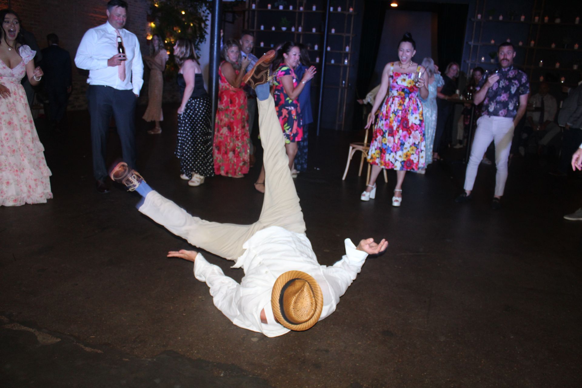 Man performing a breakdance move on a dance floor, surrounded by applauding wedding guests.