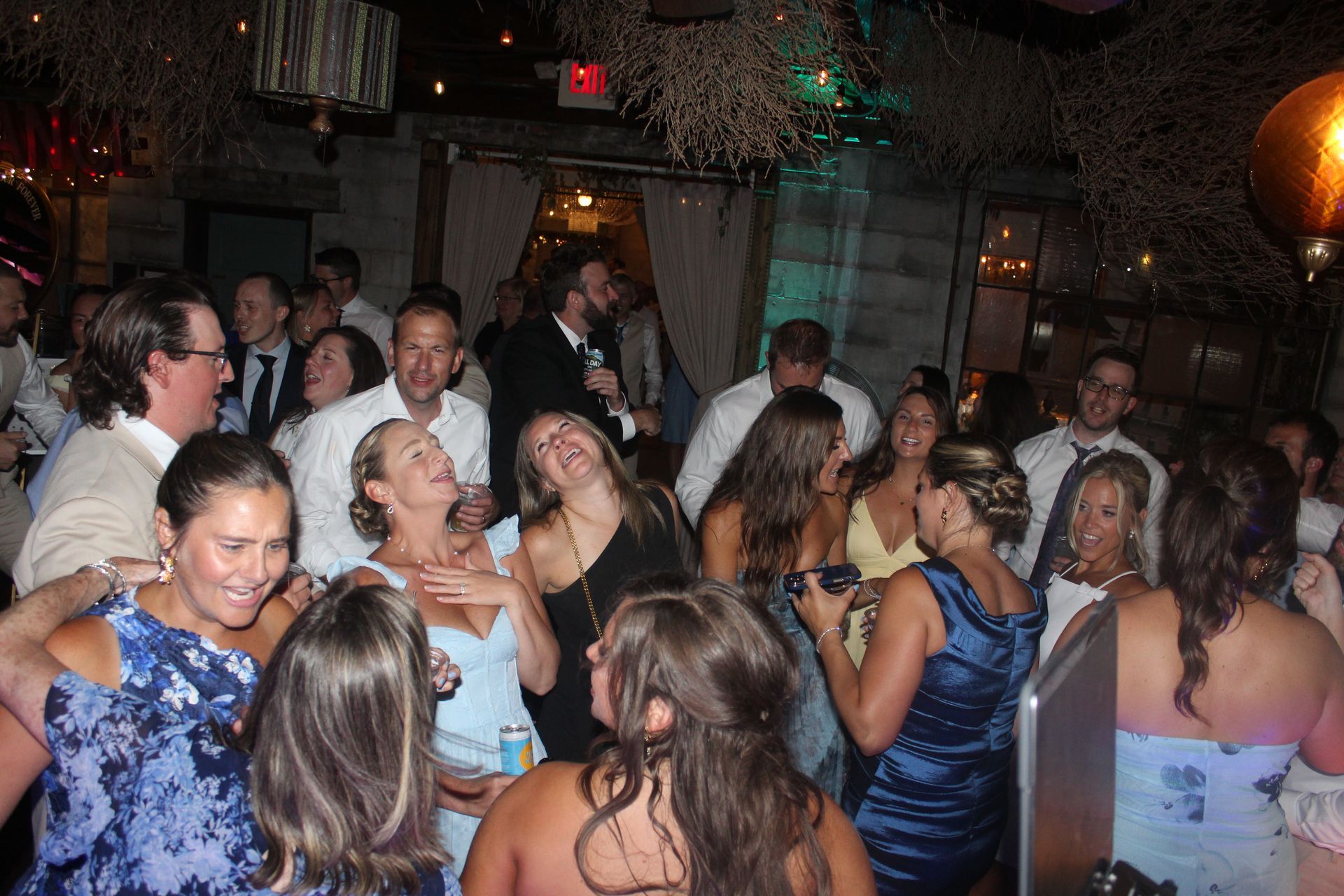 People dancing at a party in a dimly lit venue; many are laughing and enjoying themselves.
