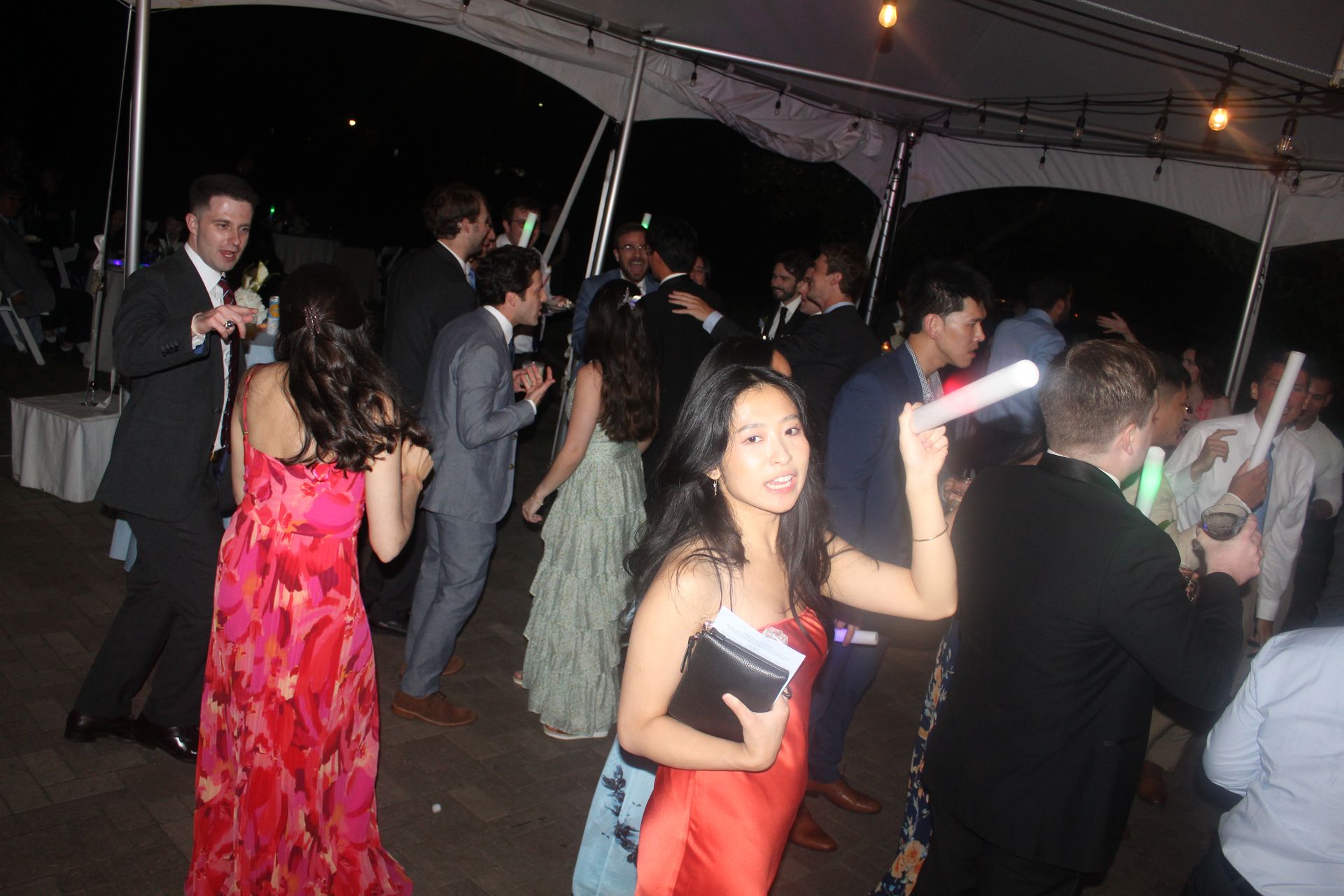 People dancing at night under a tent, some holding glow sticks.