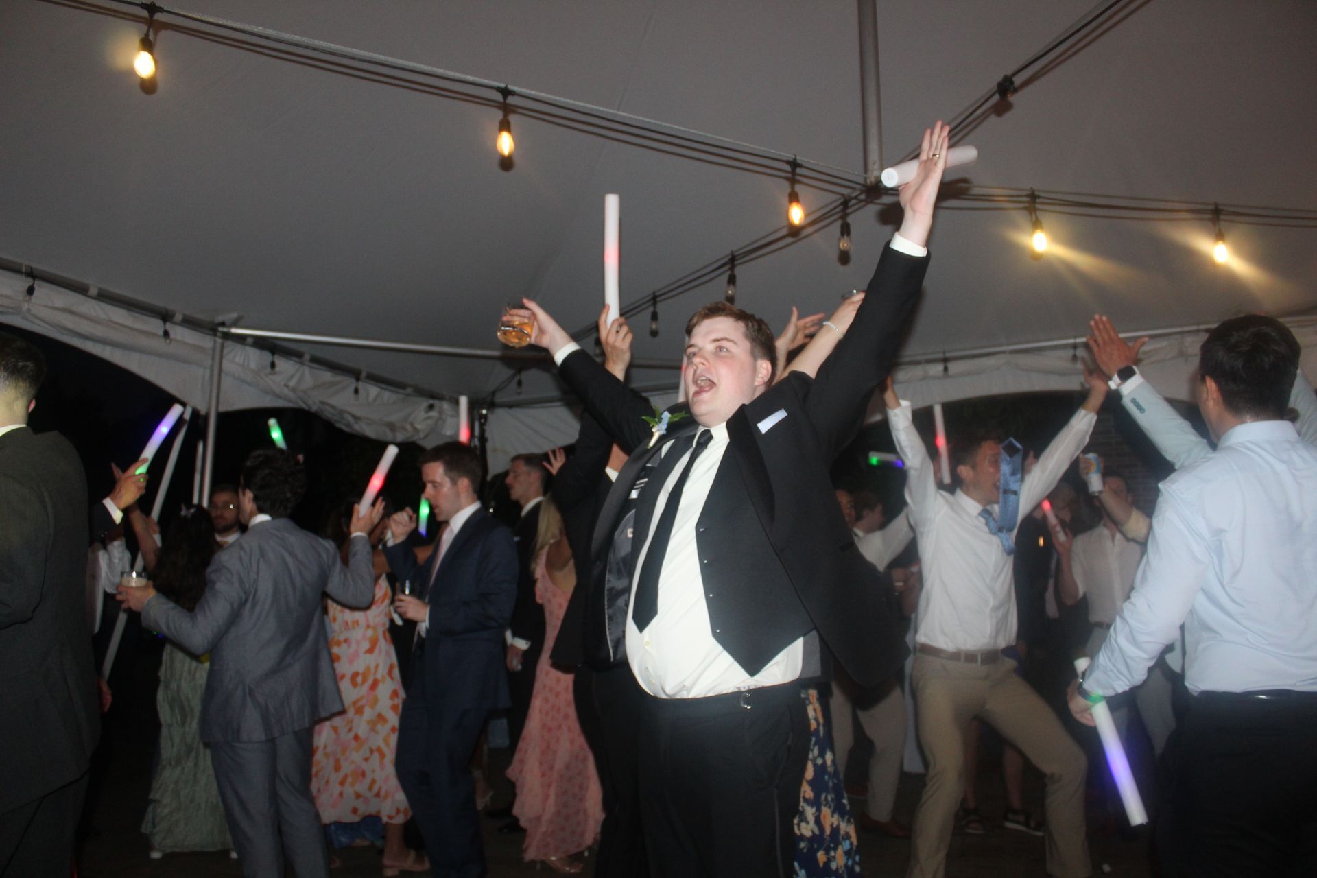 People dancing under tent, holding glow sticks, some with arms raised in celebration.