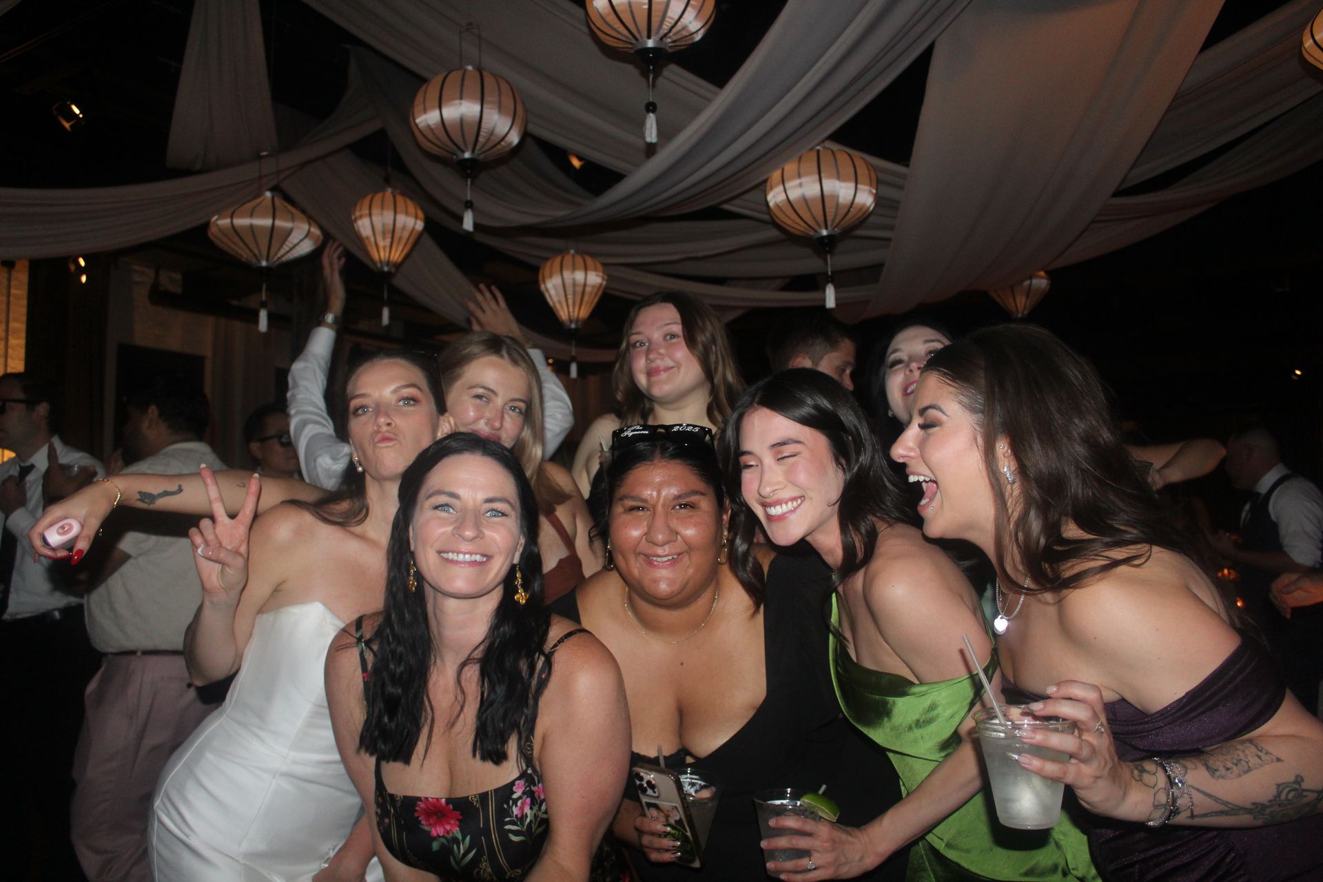 Group of people smiling, posing for a photo at a dimly lit event with hanging decorations.