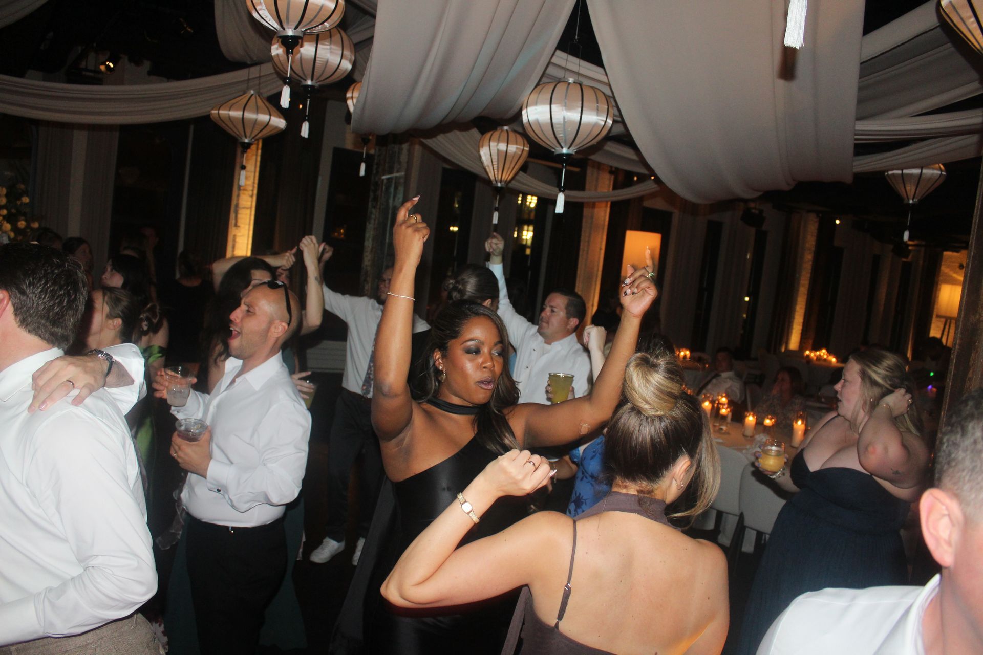 People dancing at a party under hanging lanterns, lit with warm light.