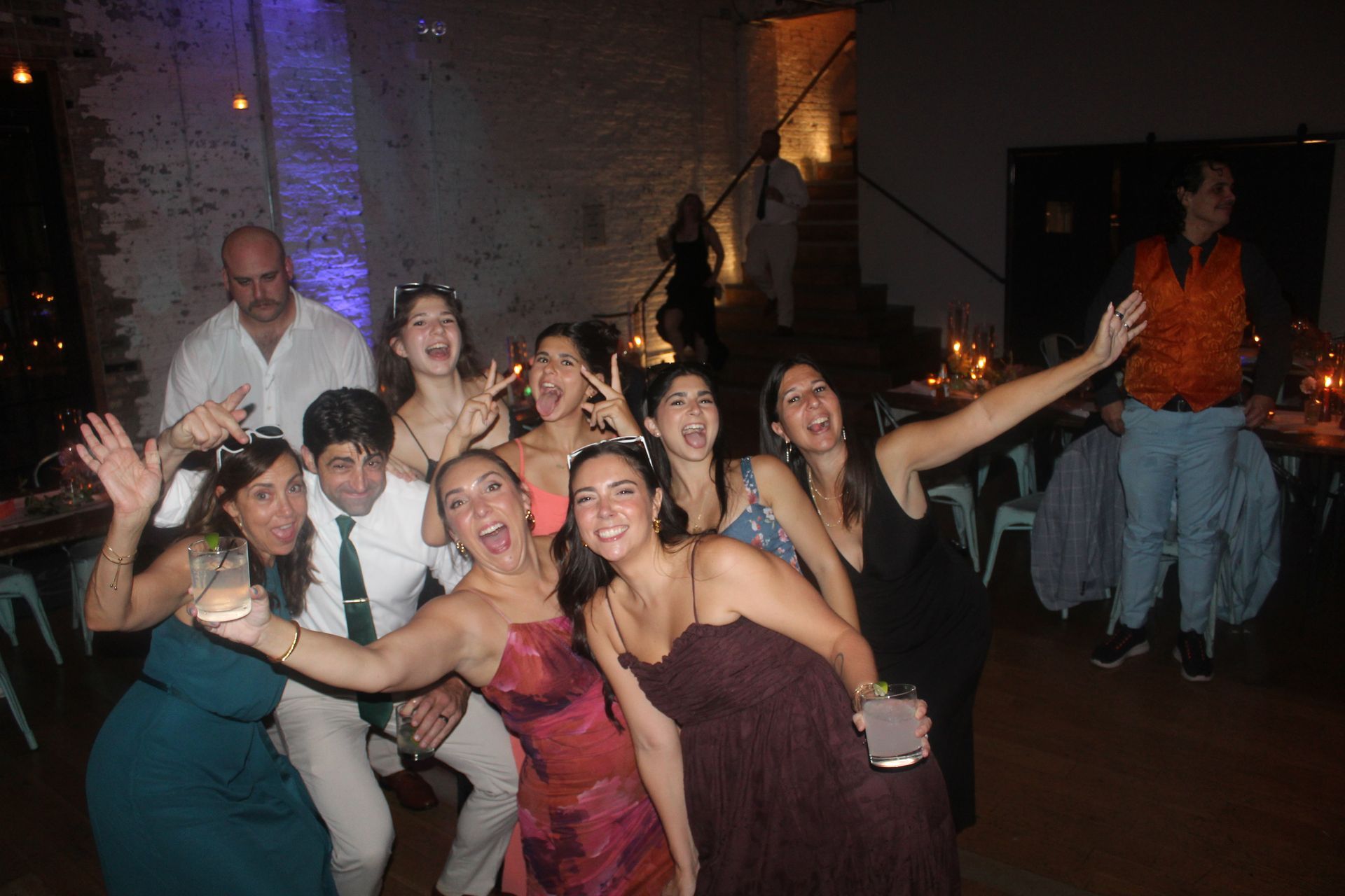 Group of people celebrating indoors, some smiling and posing, bright lighting.