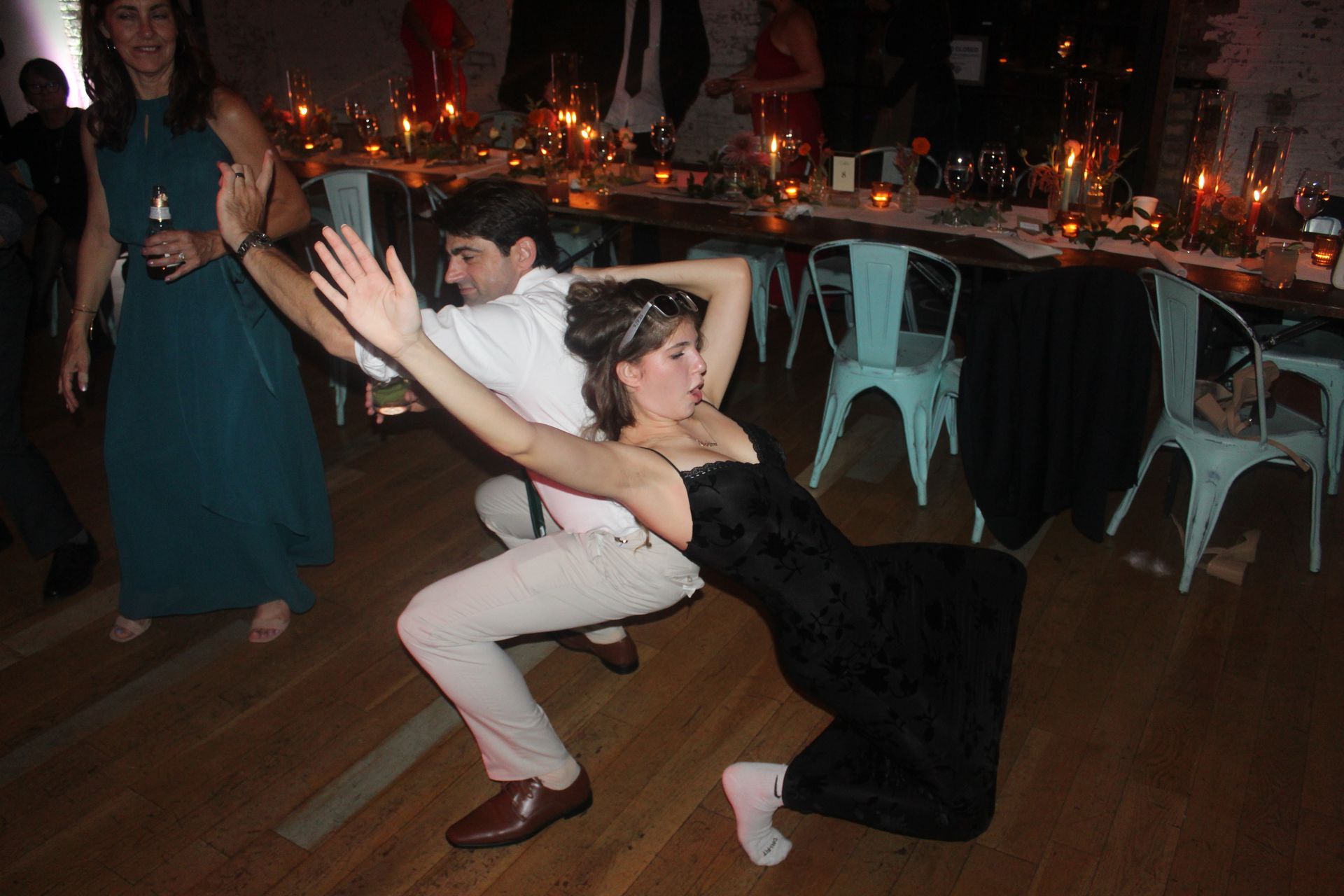 Couple dancing energetically on a wooden floor at a party; woman in black dress leaning back.