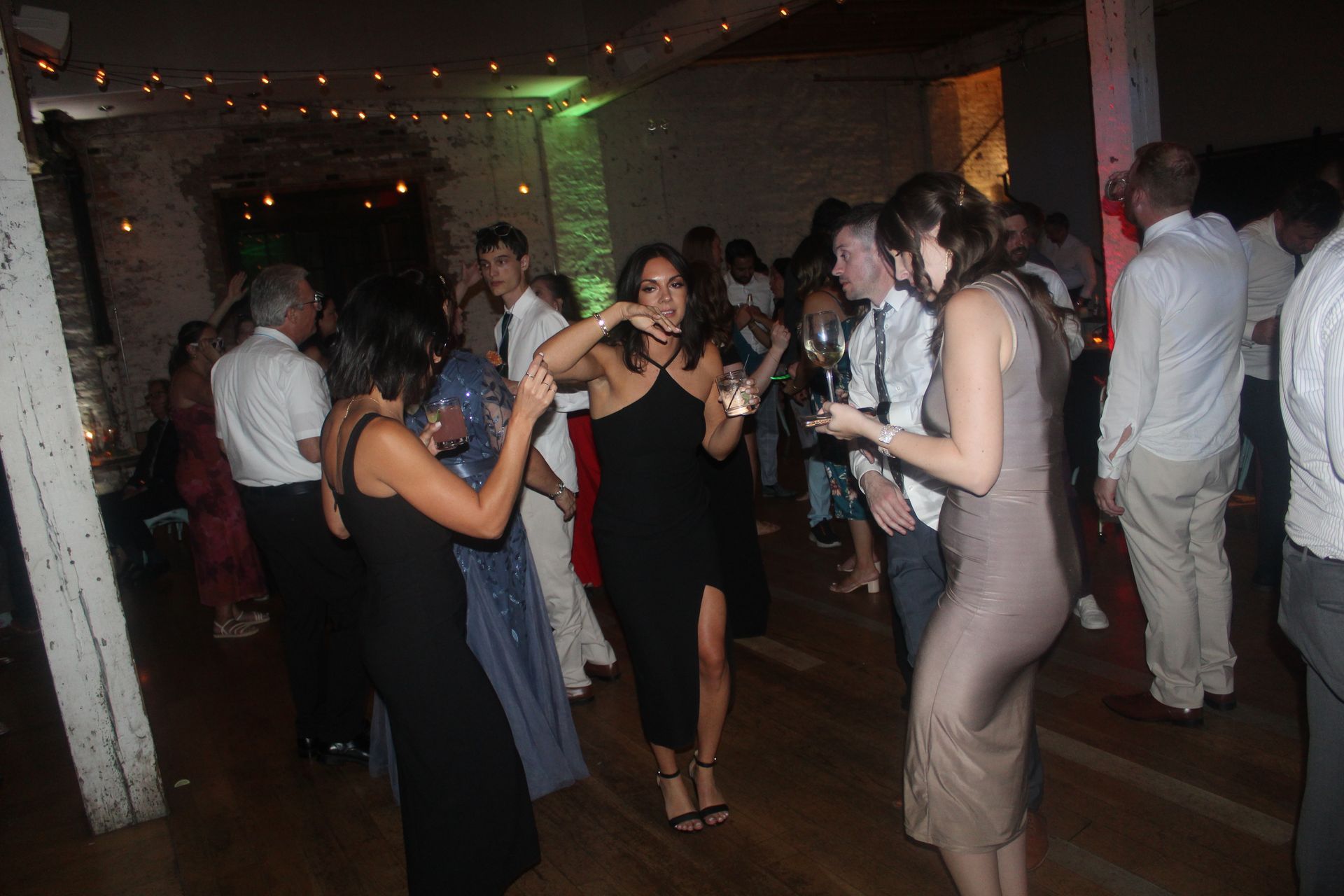 People dancing at an indoor party, some with drinks. Dim lighting.
