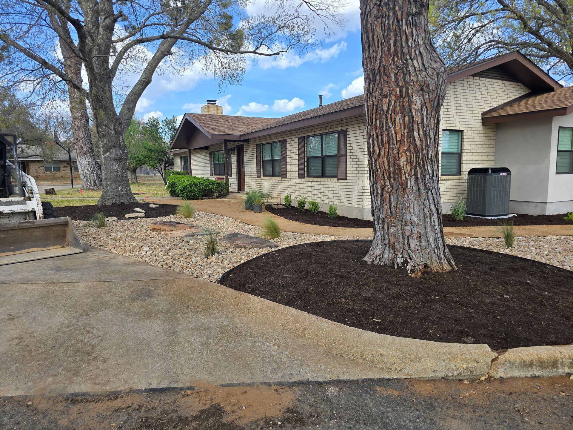 Single-story house with large trees, concrete walkway, and landscaped front yard