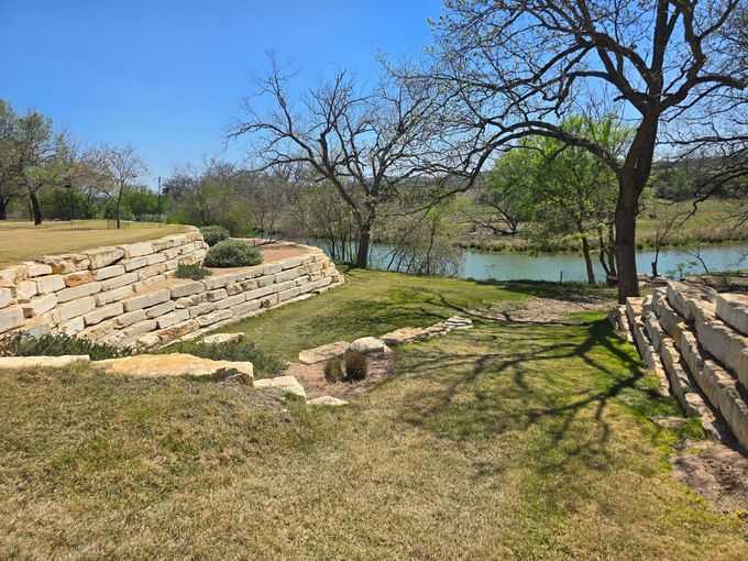 Stone ruins beside a grassy creek under leafless trees on a sunny day