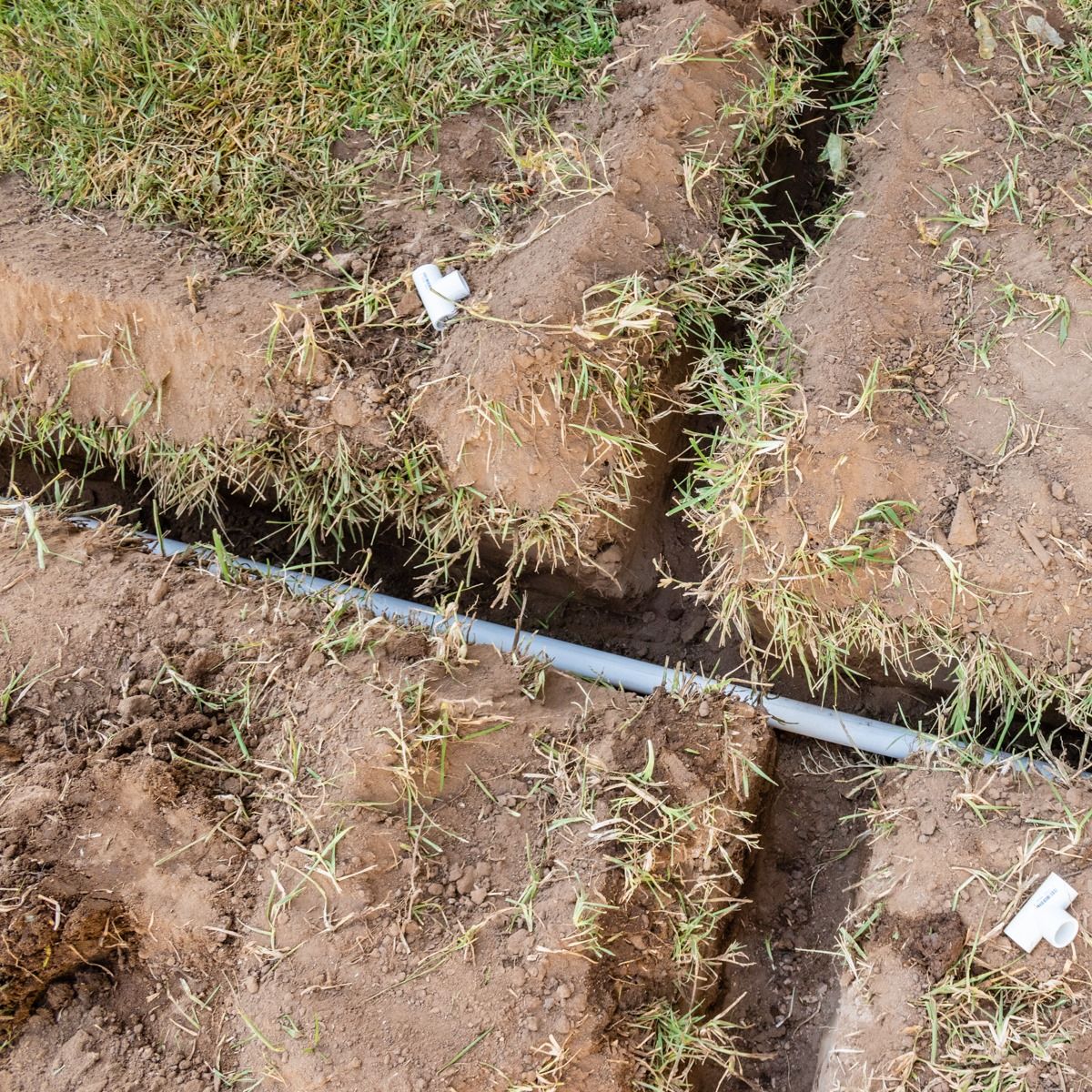 Broken gray pipe exposed in a muddy trench with grass along the edges