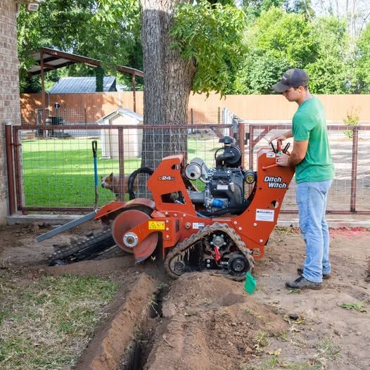 Worker operating orange trenching machine beside a tree in a yard