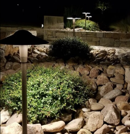 Illuminated garden path with stone retaining walls, shrubs, and a black path light at night
