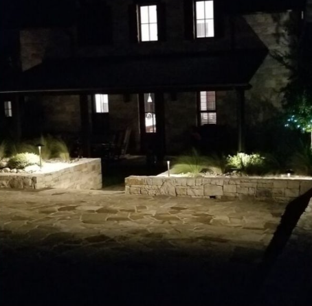 Dark stone house at night with lit windows and a stone patio in the foreground