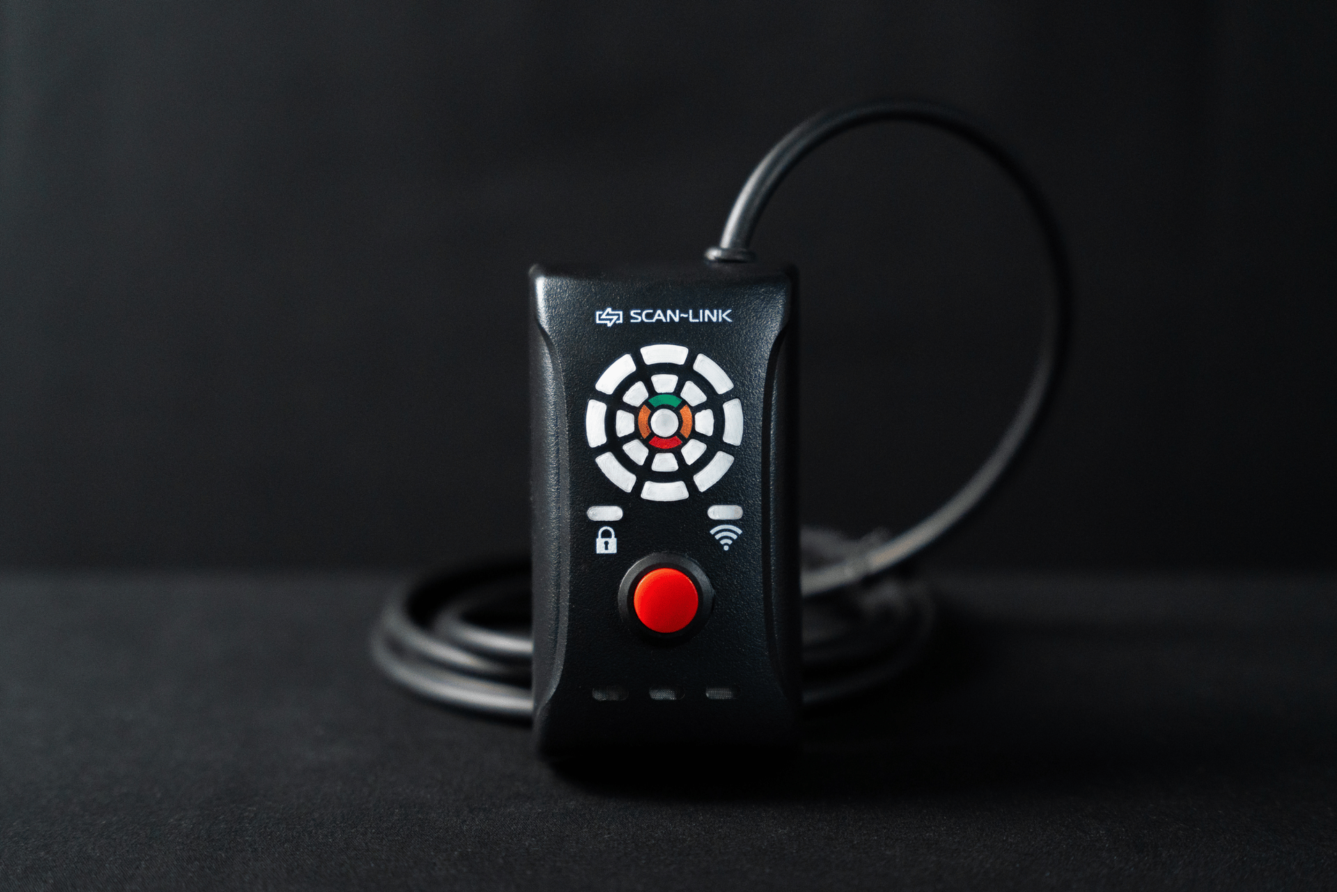 Black electronic device with a red button and dial on a dark surface.