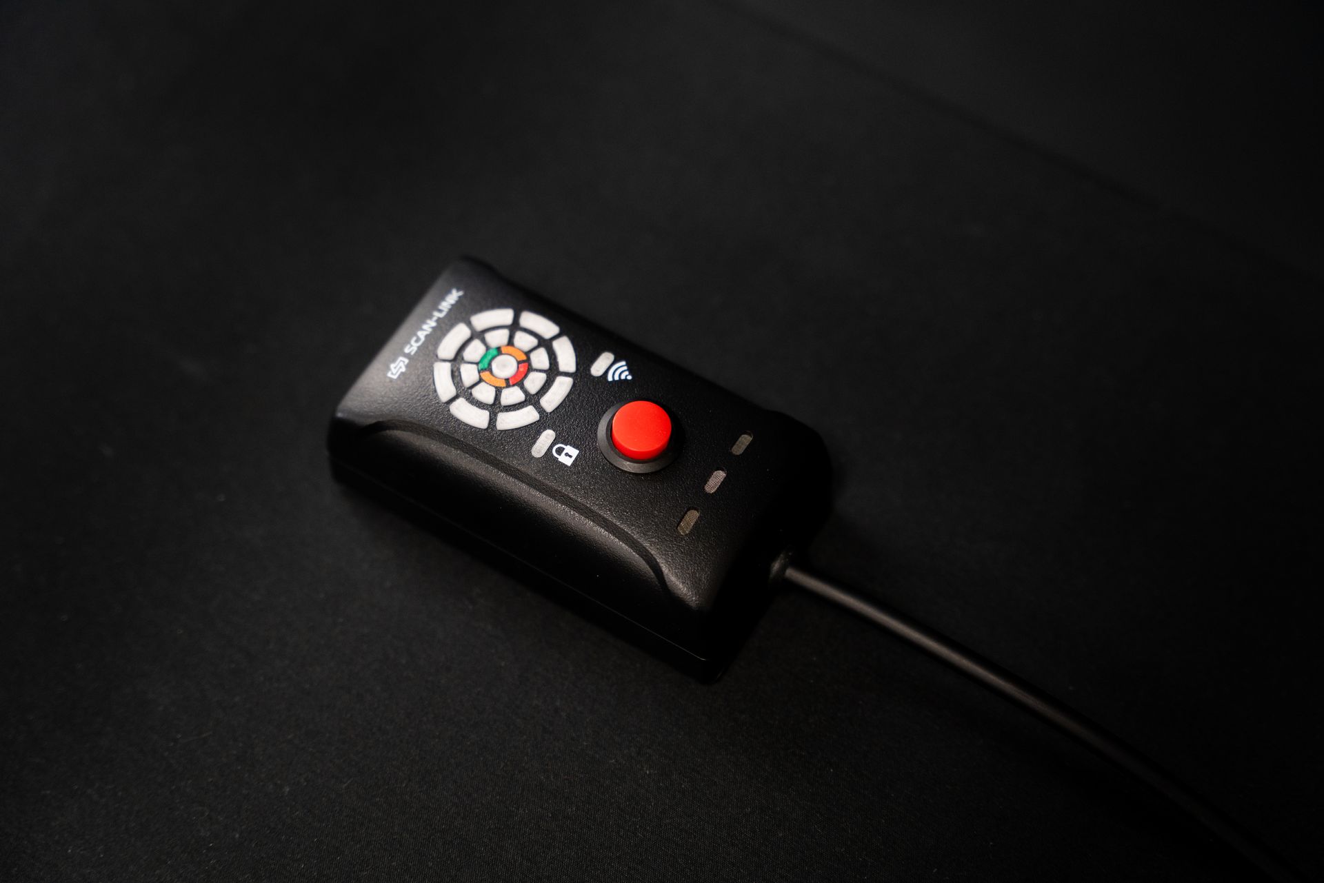 Black electronic device with a red button and dial on a dark surface.