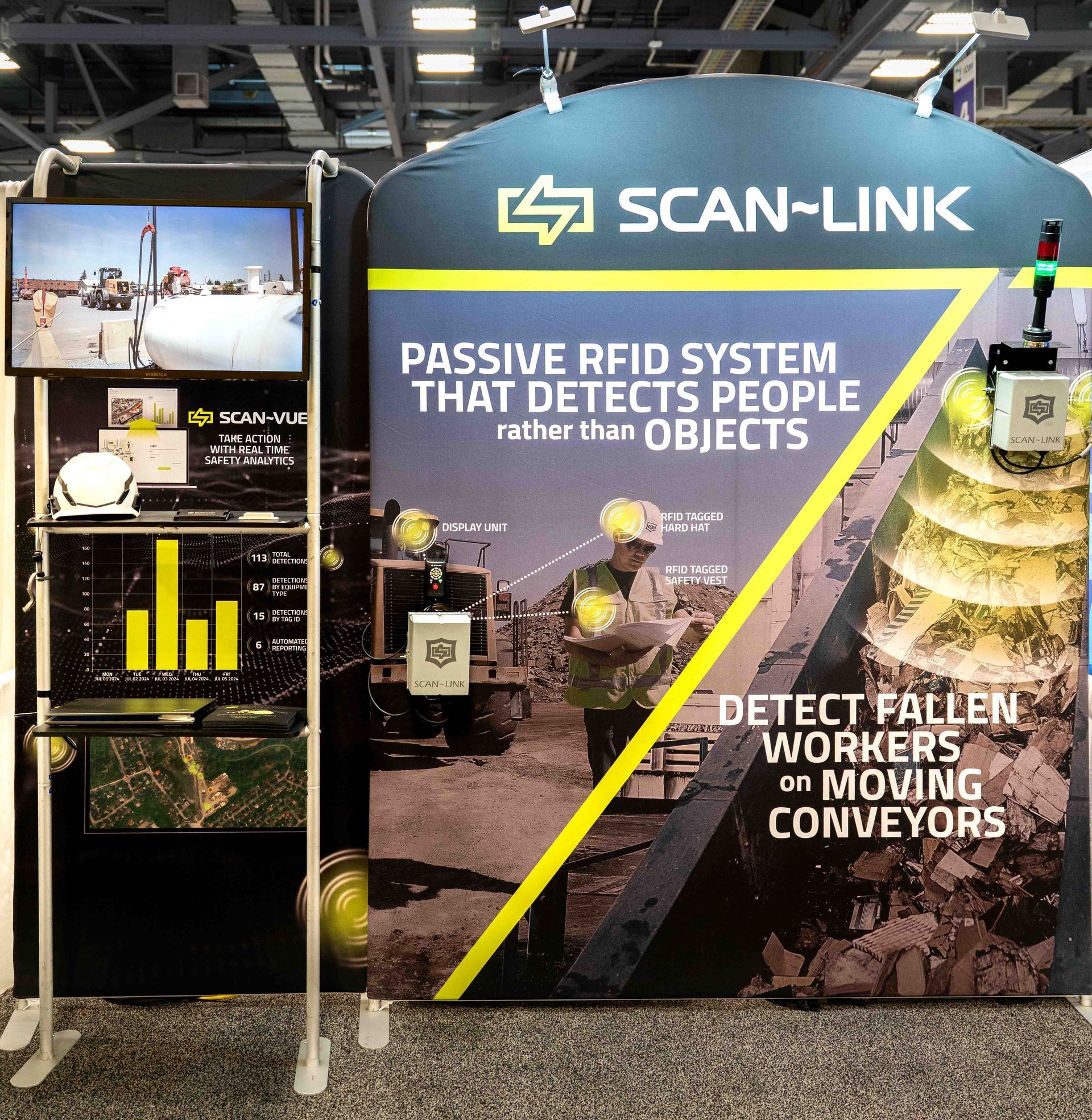 Trade show booth advertising SCAN-LINK, a passive RFID system detecting people. Text and image of a worker.