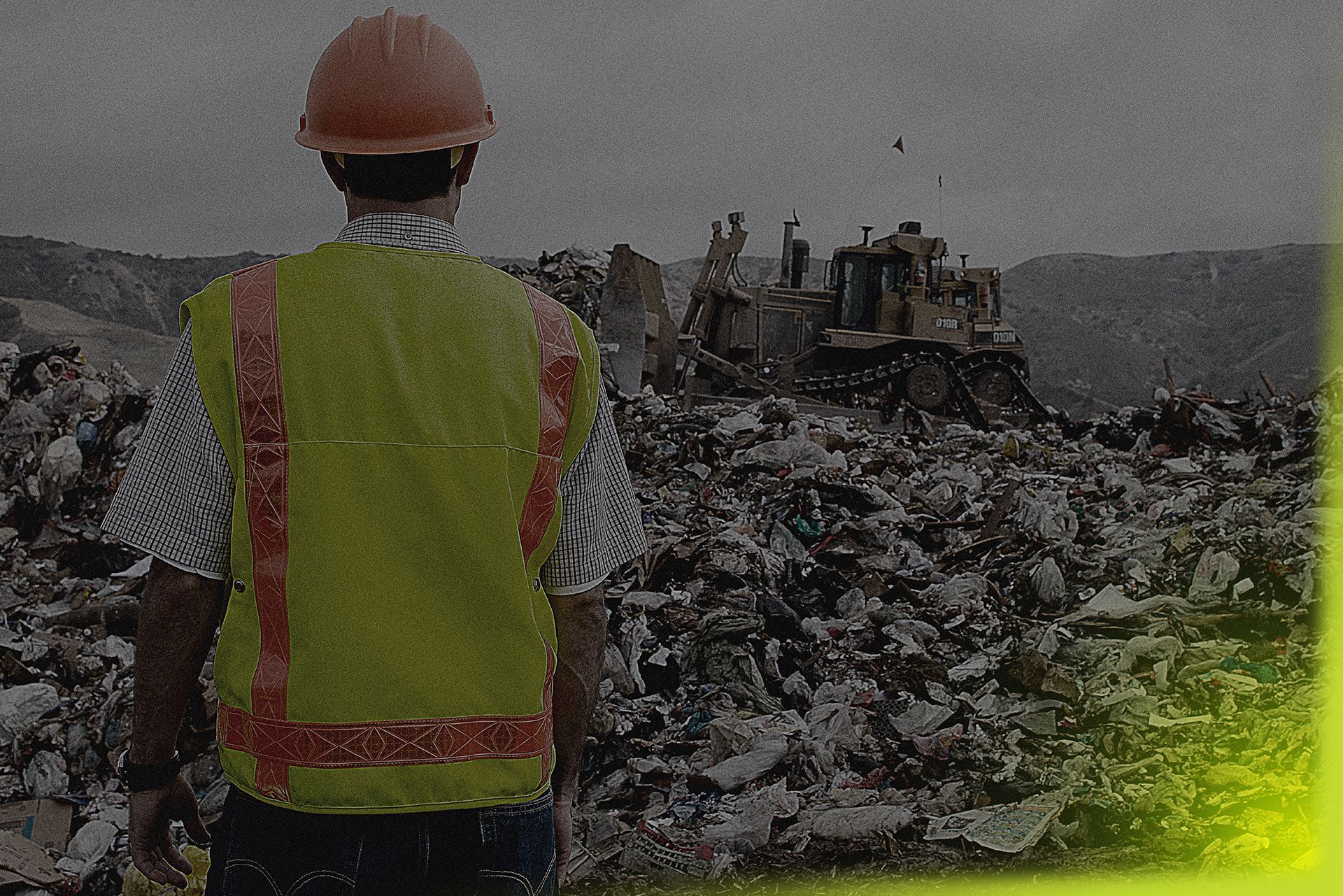 A man wearing a hard hat and safety vest is standing in front of a pile of trash.